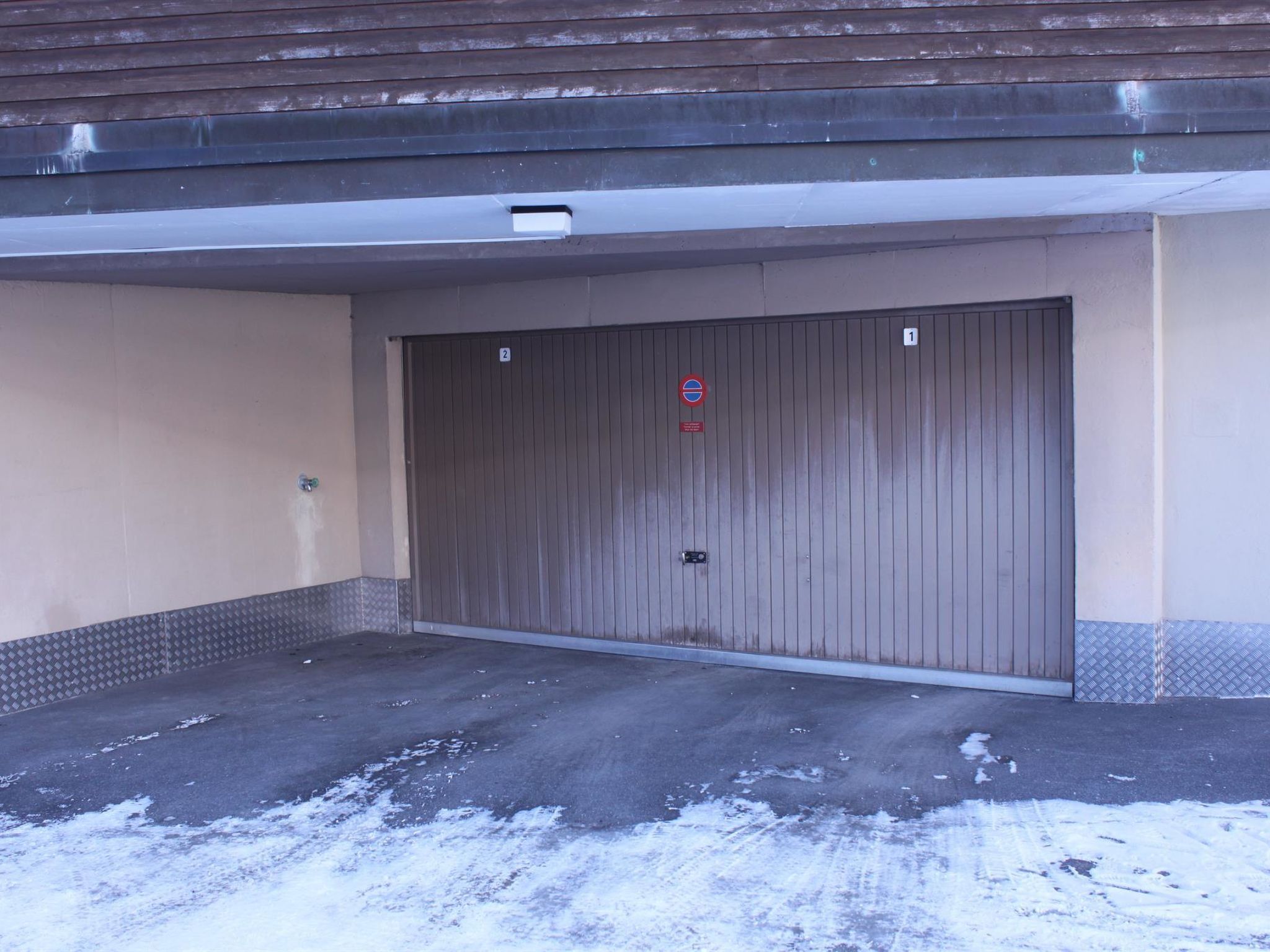 Un área de estacionamiento cercada, con una puerta metálica, un letrero de 'prohibido estacionar' y un cartel con el número 1 en la pared.