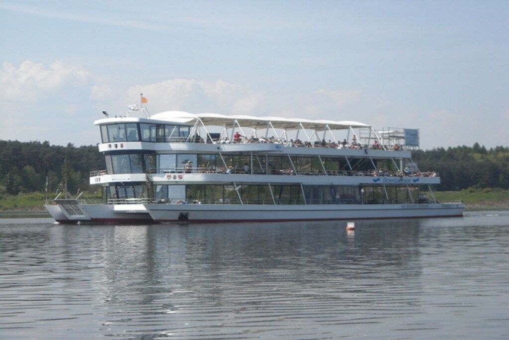 Um cruzeiro fluvial com vários decks, incluindo um deck superior coberto e uma torre de comando visível.