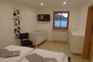 Ein Zimmer mit einem Bett, einem Babybett, einem Sessel, einem Fernseher, einem Fenster mit Aussicht und einer Heizung.