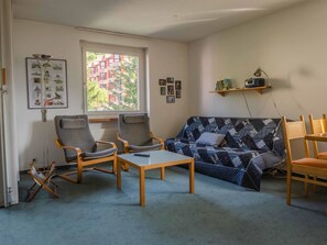 Ein Wohnzimmer mit einer Couch, zwei Sesseln, einem Couchtisch und einem Fenster mit Blick auf Gebäude.