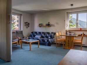 Sala de estar com sofá, cadeiras, mesa e janela com vista.