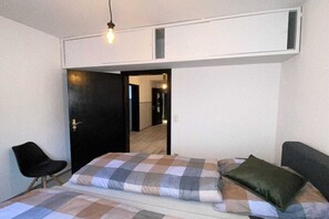 A bedroom with a bed, a chair, a door, and a light fixture. - Rumble in the Jungle (Oestrich-Winkel)
