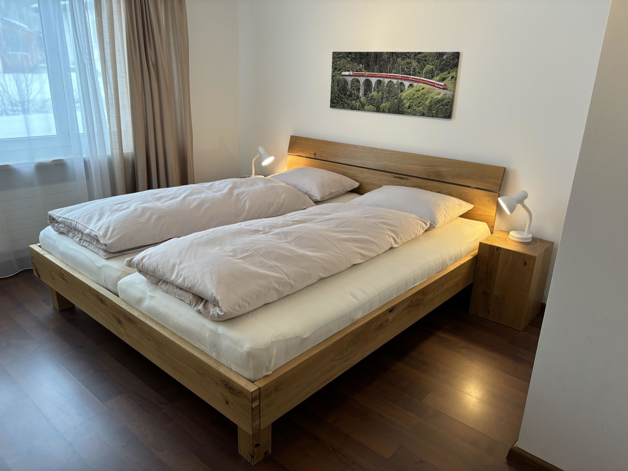Un letto matrimoniale con cornice in legno, due comodini con lampade e un quadro raffigurante un ponte appeso al muro.