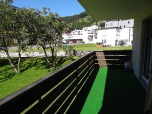 A balcony with a green carpet, a stone wall, and a view of a residential area with houses and trees. - Chesa Plonta Appartement/Fewo, Dusche oder Bad, WC 3½-Zimmerwohnung by Interhome (Davos)