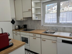 A compact kitchen with a built-in oven, a sink, and a window with a view of a snowy landscape. - Chesa Plonta Appartement/Fewo, Dusche oder Bad, WC 3½-Zimmerwohnung by Interhome (Davos)