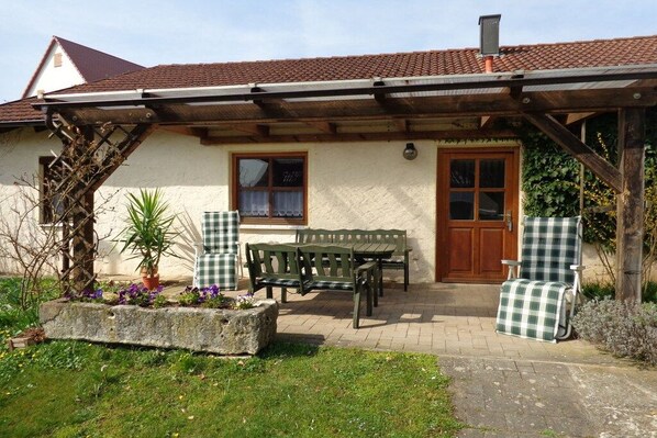 Ein Haus mit einer überdachten Terrasse, einer hölzernen Bank, einem Tisch und einem Stuhl.