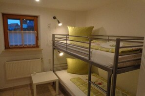 Quarto com beliche, janela, radiador e mesa de cabeceira.