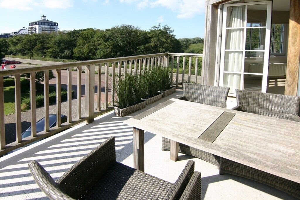 A balcony with wicker furniture, a view of the road, and a building in the background.