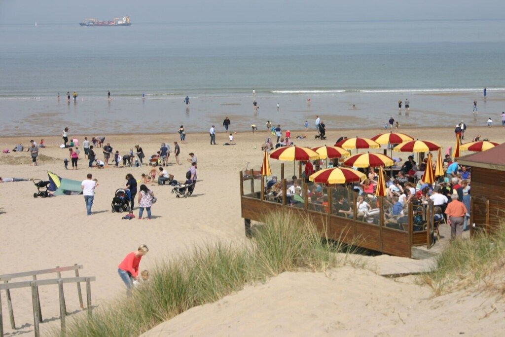 Une plage avec des gens, des parasols et une structure en bois.