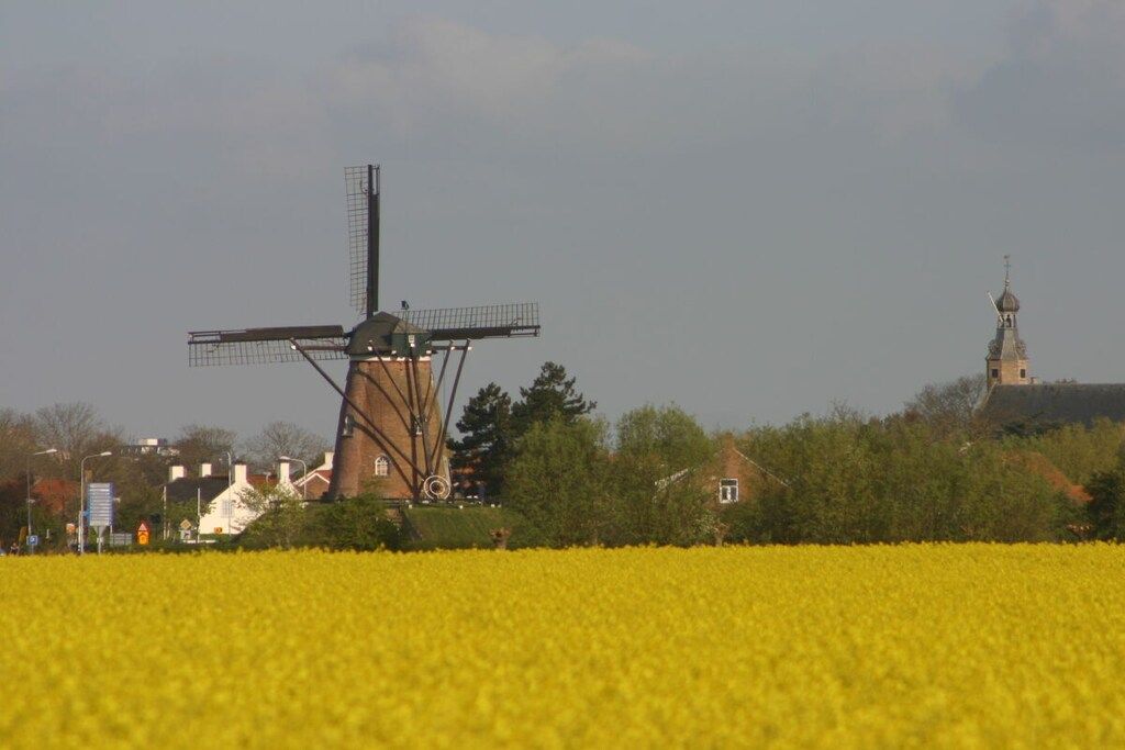 Eine Windmühle in einem Feld, im Hintergrund eine Kirche.
