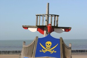 Eine Holzkonstruktion mit Totenkopf- und Knochensymbol, einem rot-weißen Sonnenschirm und einem Metallstab.