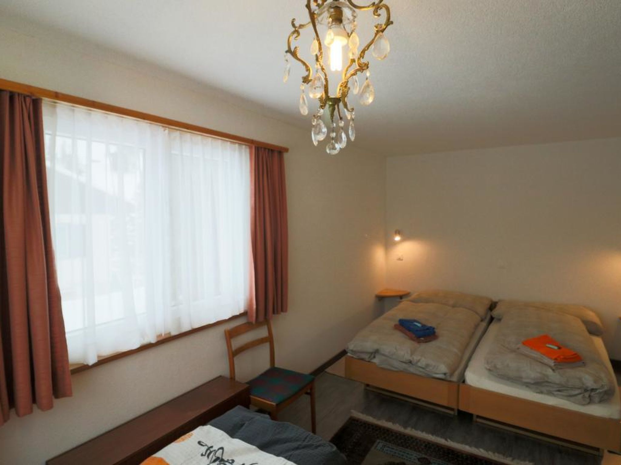 A bedroom with a single bed, a chair, a small table, and a window with curtains.