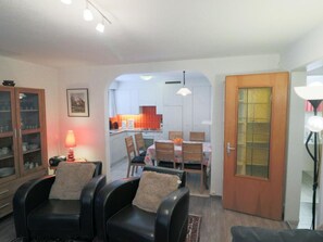 Ein Wohnzimmer mit Essbereich, einer Küche im Hintergrund und einer Holztür.