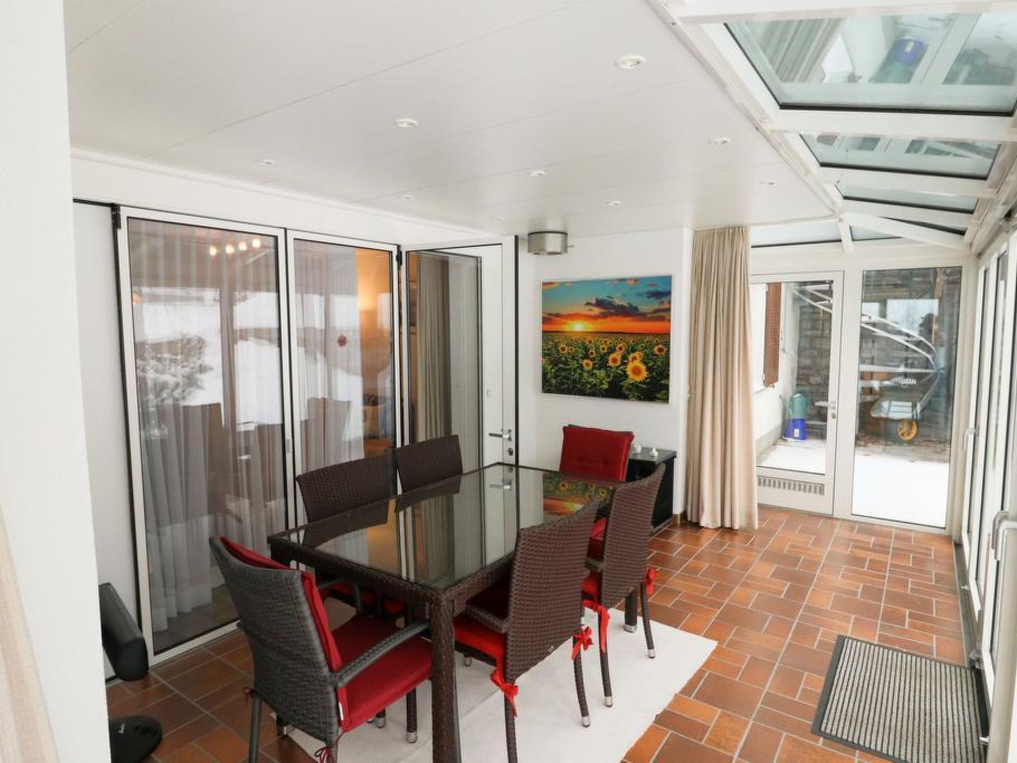 Un coin repas avec une table et des chaises en verre, un tableau au mur et une vue à travers les portes vitrées.