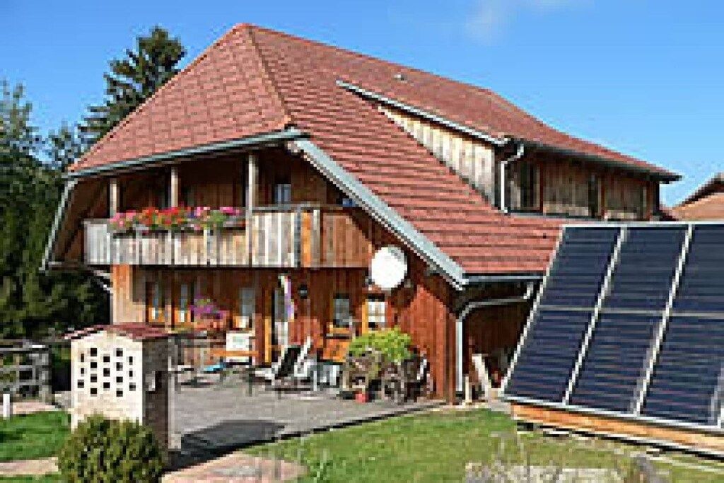 Ein zweigeschossiges Haus mit einem geneigten Dach, einem Balkon mit Pflanzen und einer Anlage von Solarmodulen.
