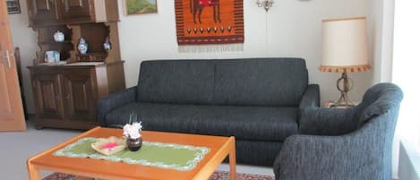 A living room with a sofa, a small table with a vase, a cabinet, and a wall-mounted lamp.