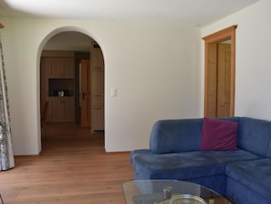 A living room with a blue sofa, a glass coffee table, and an arched doorway leading to a kitchen. - Sunna Büel Appartement/Fewo, Dusche oder Bad, WC 2½-Zimmerwohnung by Interhome (Davos)
