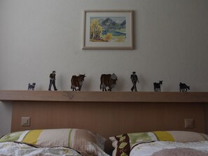 Quarto com cama, almofadas, uma estante com figuras e um quadro na parede.