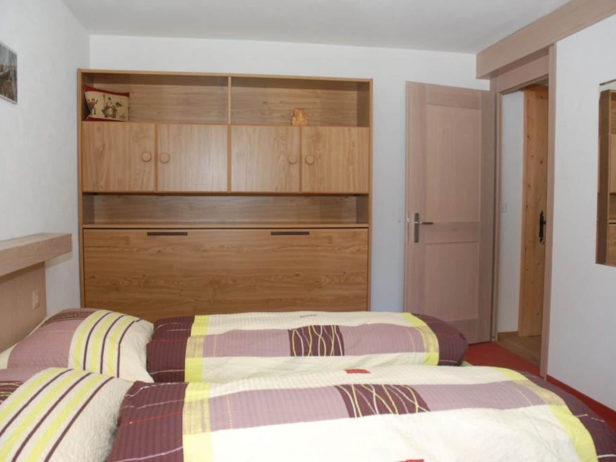 Une chambre avec une armoire en bois, un lit avec une literie à rayures et une porte donnant sur une autre pièce.