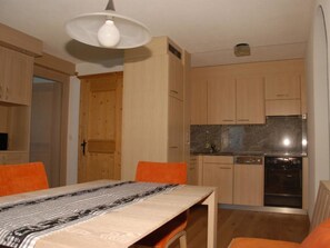 Cozinha compacta com armários de madeira, forno embutido e área de refeições com mesa e cadeiras.