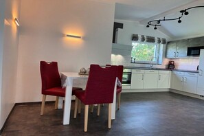 A modern kitchen with white cabinets, a dining table with red chairs, and a window providing natural light. - Schröder holiday home (Cattenstedt)
