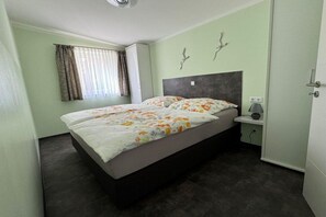 A single bed with a floral bedspread in a room with light green walls, a dark headboard, and a window with curtains. - Schröder holiday home (Cattenstedt)