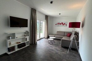 A modern living room with a flat-screen TV, a sofa, a coffee table, and a lamp. - Schröder holiday home (Cattenstedt)