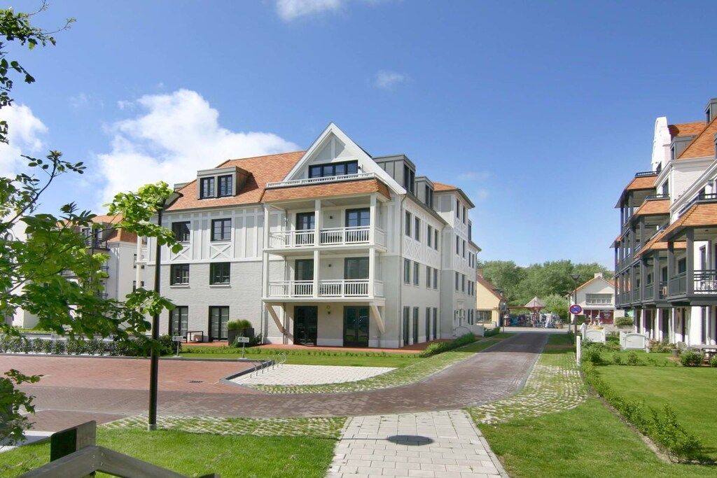 En flervåningsbostadsbyggnad med en balkong på andra våningen, en asfalterad uppfart och en välskött gräsmatta.