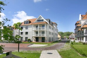 Ein mehrgeschossiges Wohngebäude mit einem Balkon im zweiten Stock, einer gepflasterten Auffahrt und einem gepflegten Rasen.