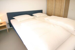 Ein ordentlich bezogenes Bett mit weißer Bettwäsche, ein hölzernes Kopfende und ein Nachttisch mit einer Lampe.