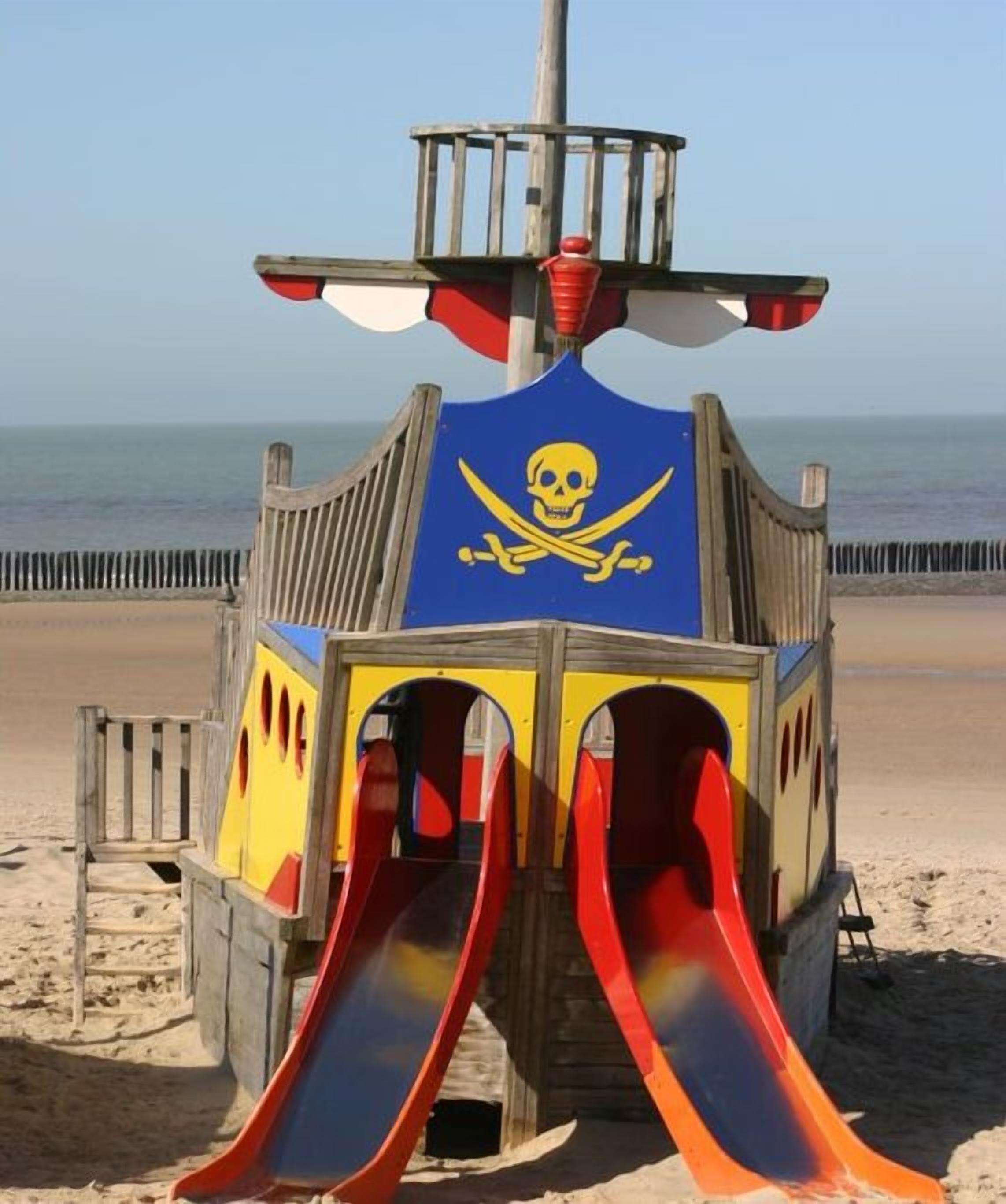 Een speelconstructie op het strand met een piratenthema, inclusief een schedel en gekruiste botten symbool, en twee glijbanen.