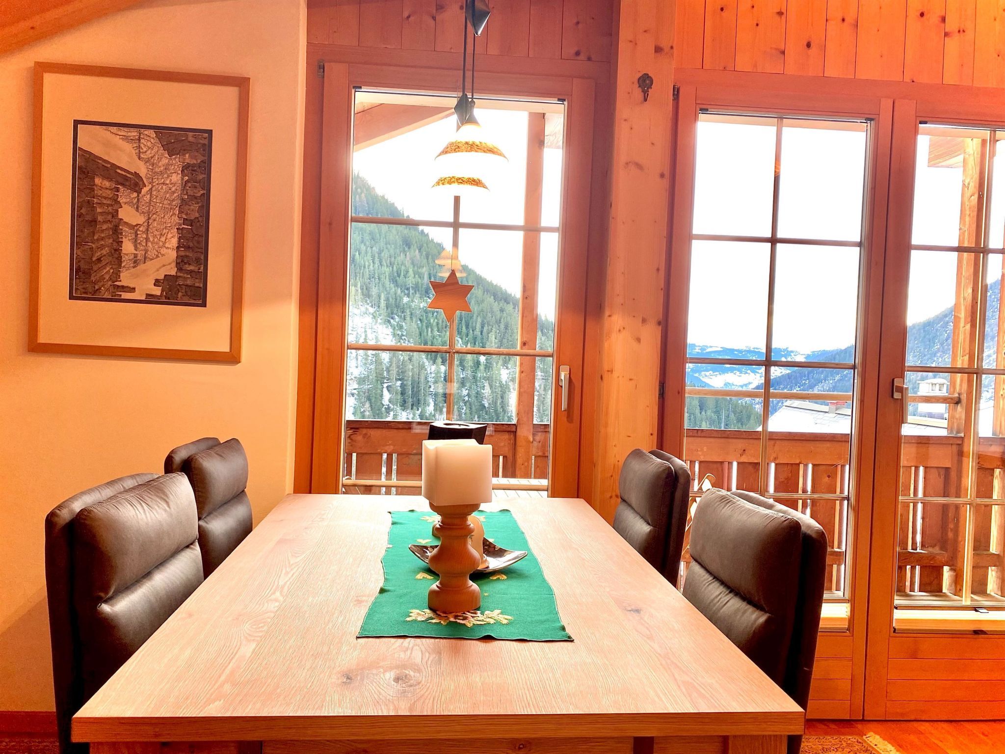 Ein Holztisch mit vier Stühlen, einer Kerze und einem gerahmten Bild an der Wand.