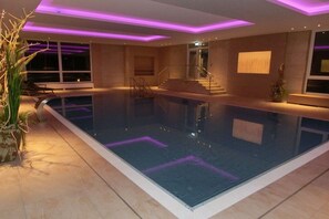 Ein moderner, überdachter Schwimmbereich mit Glasbarriere, Treppe und stimmungsvoller Beleuchtung.