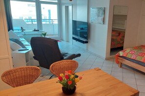 Ein modernes Wohnzimmer mit einer Couch, einem Esstisch mit Stühlen, einem Fernseher und einem Bett mit einer farbenfrohen Decke.
