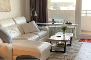A modern living room with a sofa, a coffee table, and a view of the outside through a window. - Luca Panorama Apt. 74, 5th floor (Cuxhaven)