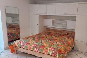 A bedroom with a bed, a wooden headboard, a white wardrobe with multiple compartments, and a mirror. - Luca Panorama Apt. 74, 5th floor (Cuxhaven)