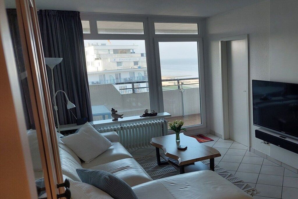 A hotel room with a balcony, a sofa, a TV, and a view of the sea.