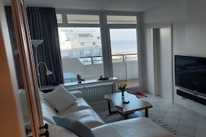 Habitación de hotel con balcón, sofá, televisión y vistas al mar.