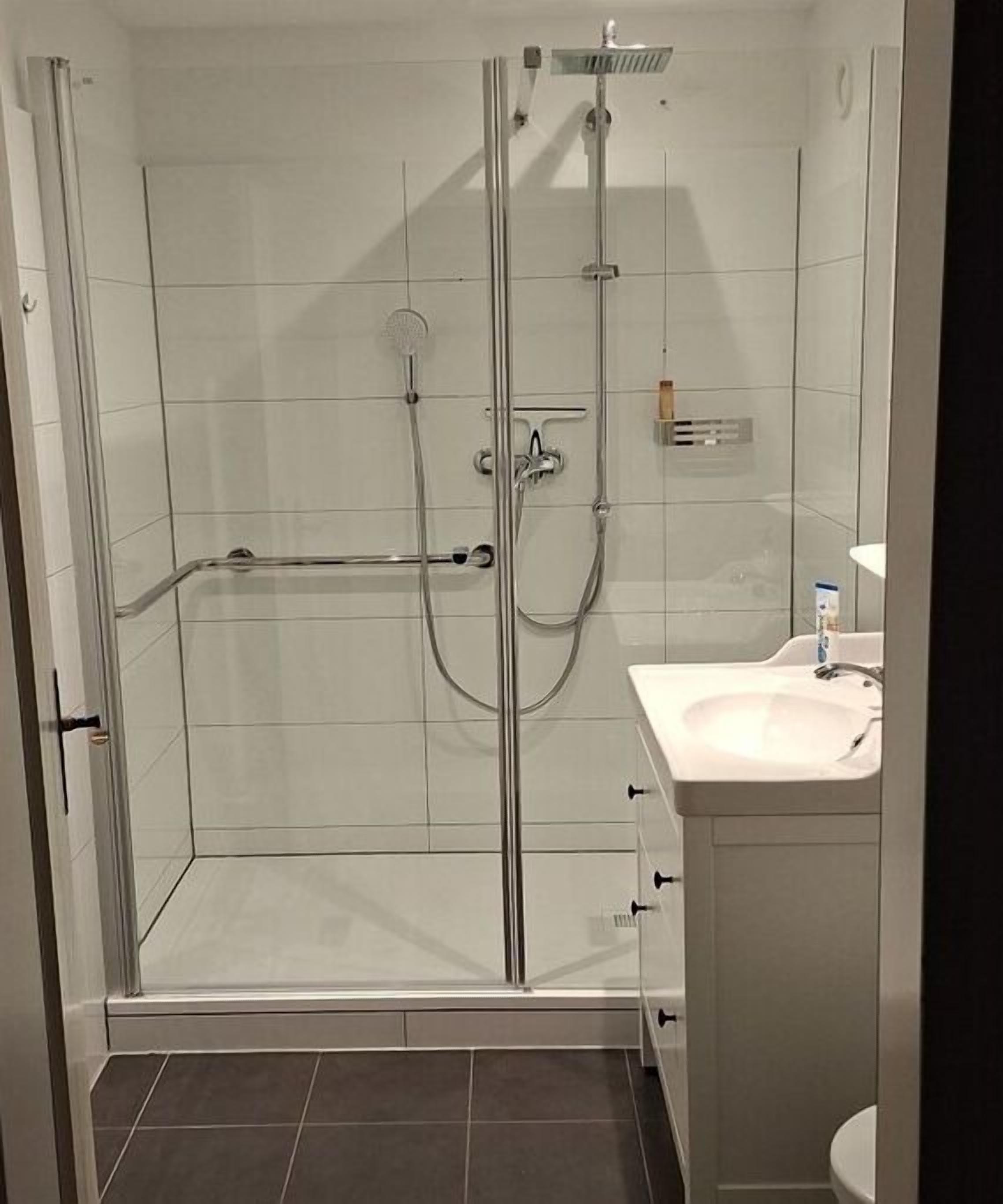 A glass-enclosed shower with a handheld showerhead, a handheld showerhead, and a wall-mounted faucet.