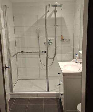 Eine Duschkabine mit einer Handbrause, einer weiteren Handbrause und einem am Wand befestigten Wasserhahn.