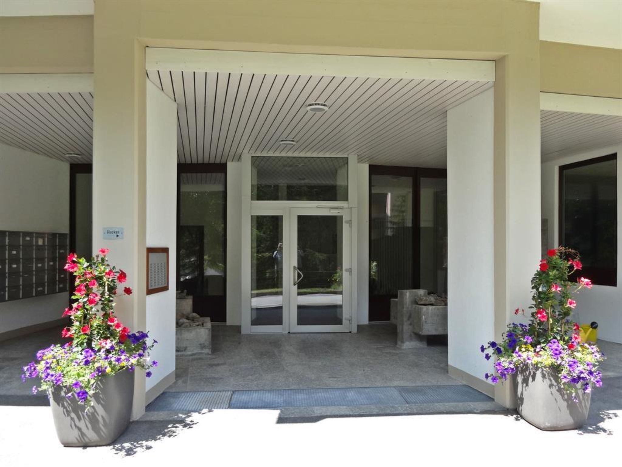 Entrada d'hotel amb porta de vidre, plantes en testos i un senyal que indica el camí a la llotja.