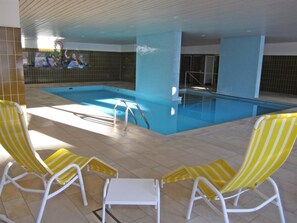 Una piscina interior amb dues gandules grogues i una taula petita.