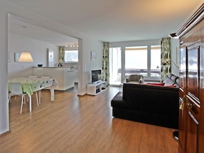 A modern living room with a sofa, a dining area with a table and chairs, a kitchen area, and large windows. - Residenz im Park Whg Alpenblick Appartement/Fewo, Dusche oder Bad, WC by Interhome (Davos)