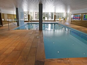 An indoor swimming pool with tiled flooring and a central column, surrounded by windows and a tiled wall. - Residenz im Park Whg Alpenblick Appartement/Fewo, Dusche oder Bad, WC by Interhome (Davos)