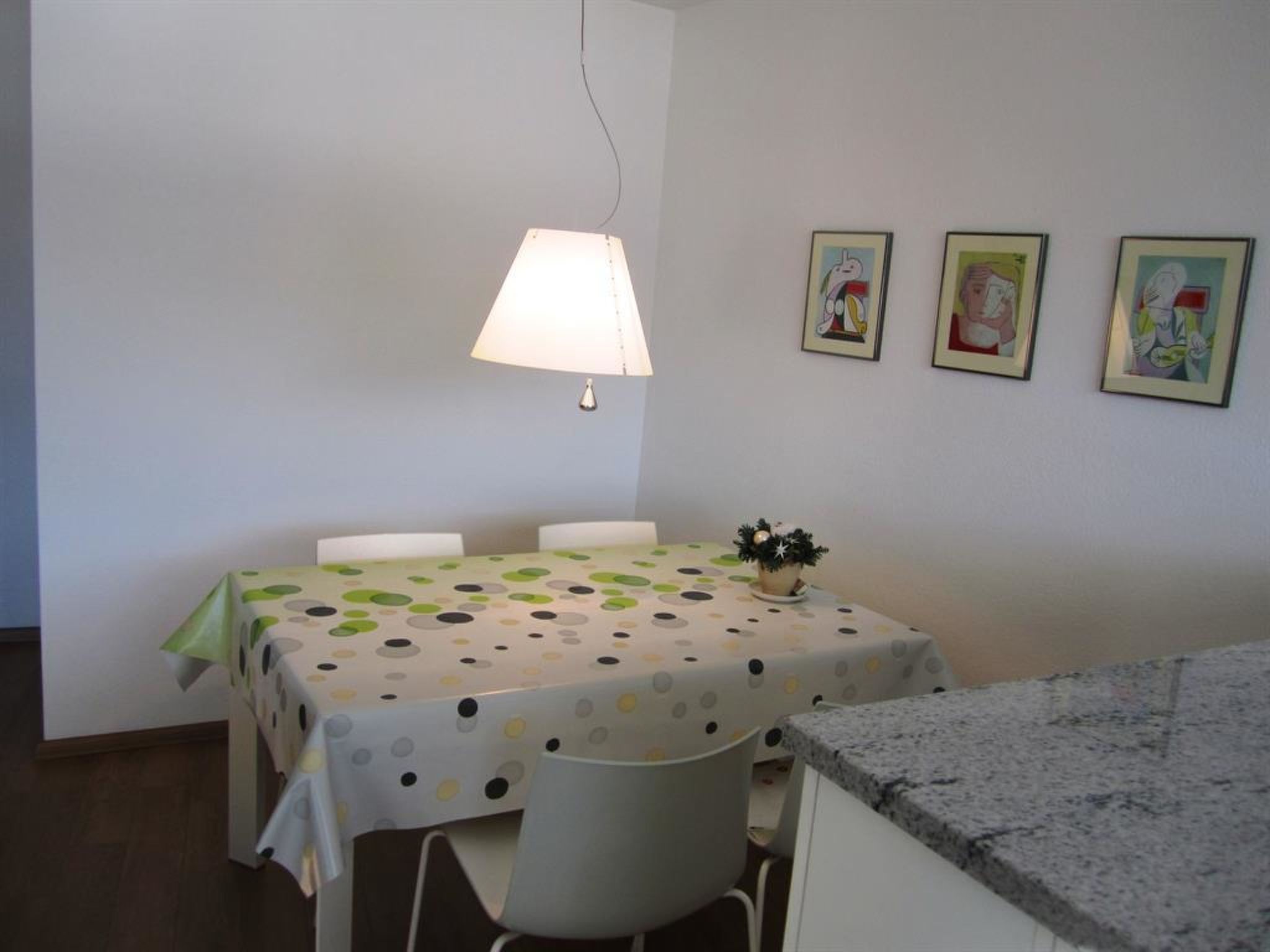 Ein Essbereich mit einem Tisch, der mit einer Tischdecke mit Punkten bedeckt ist, einer Hängelampe und drei gerahmten Kunstwerken an der Wand.