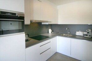 A modern kitchen with white cabinets, a built-in oven, a sink, and a coffee maker. - Beach Residence A302 (Cadzand)