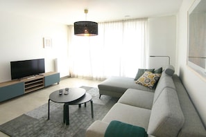 A modern living room with a flat-screen TV, a round coffee table, a grey sofa with a patterned throw, and a pendant light. - Beach Residence A302 (Cadzand)