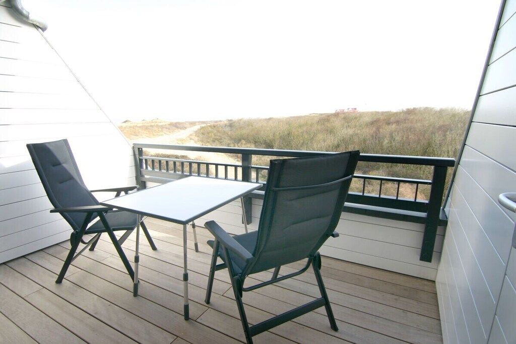 Een balkon met een tafel en twee stoelen, met uitzicht op een strand.