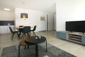 A modern living room with a flat-screen TV, a dining area with chairs, and a kitchen in the background. - Beach Residence A302 (Cadzand)