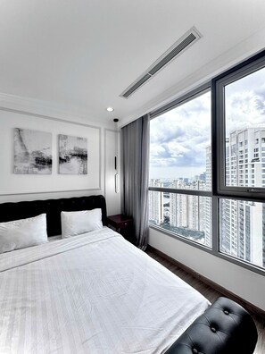 Habitación de hotel moderna con una cama grande, vista panorámica de la ciudad y dos obras de arte abstracto en la pared.